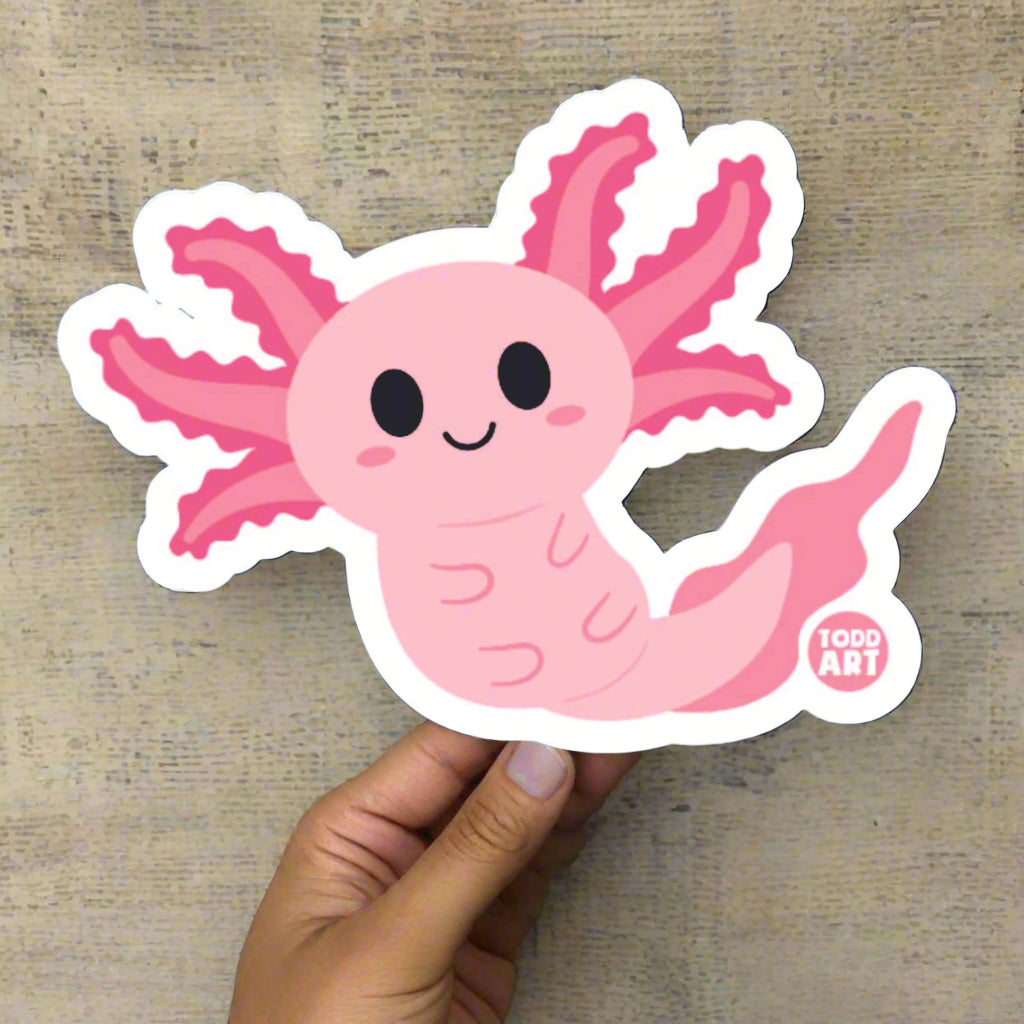 Hand holding a large Boo-Boo Buddies® collectible axolotl vinyl sticker with cute pink gills and smiley face against a neutral background