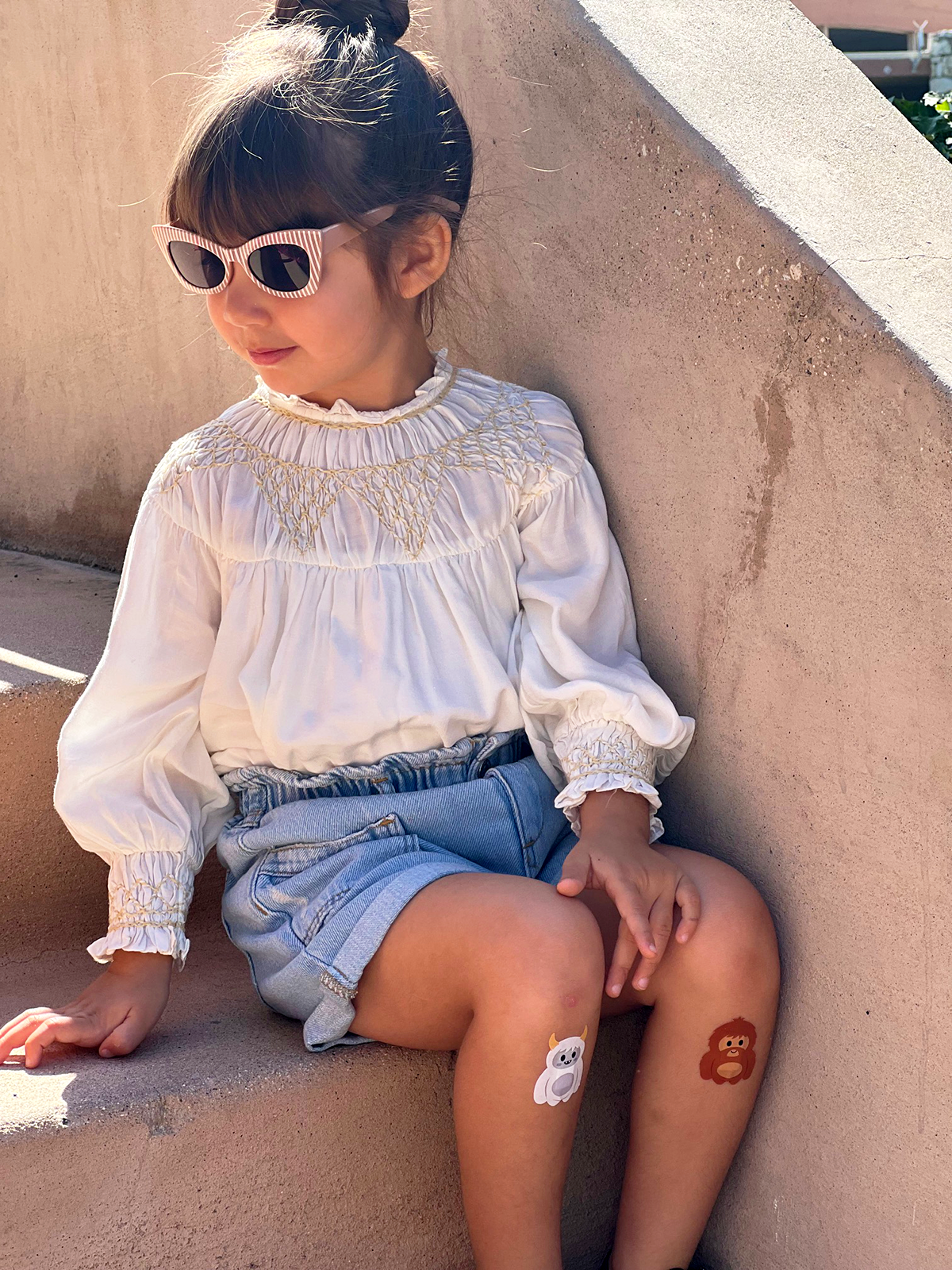Girl sitting on steps wearing Boo-Boo Buddies® Bigfoot and Yeti bandages on knees – fun monster-themed kids bandages for summer adventures and outdoor play