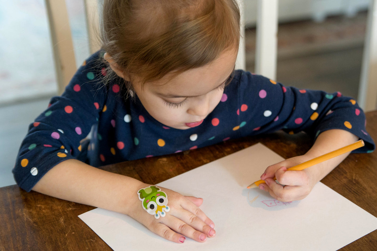 Child drawing at a table while wearing a Boo Boo Buddies fun and colorful kids bandage on her hand.
