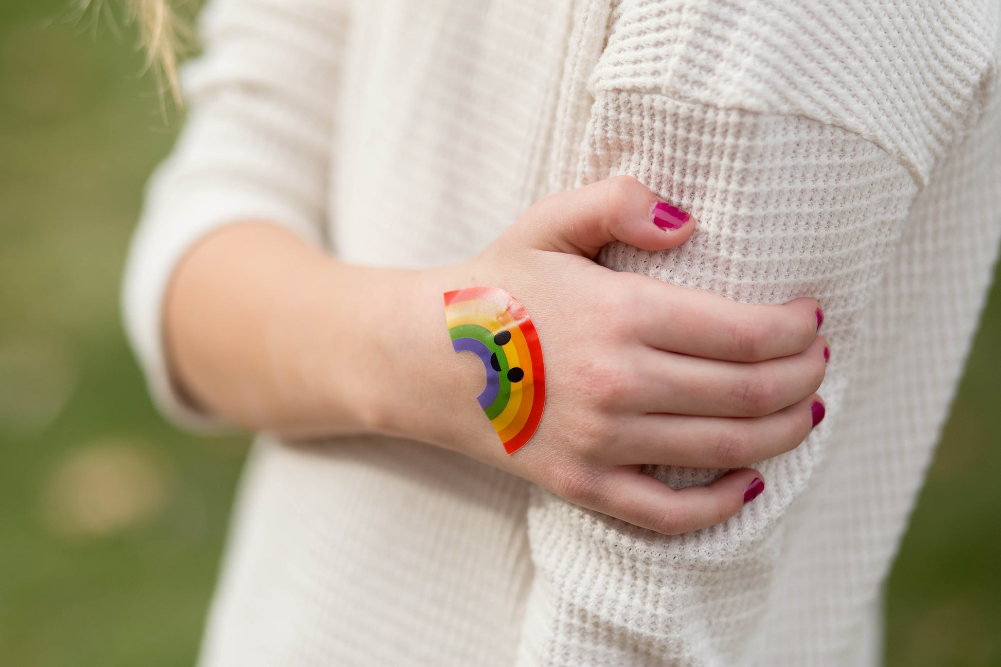 Closeup of Boo Boo Buddies rainbow bandage on hand, bright cheerful bandaid for kids that adds color and comfort to minor scrapes.
